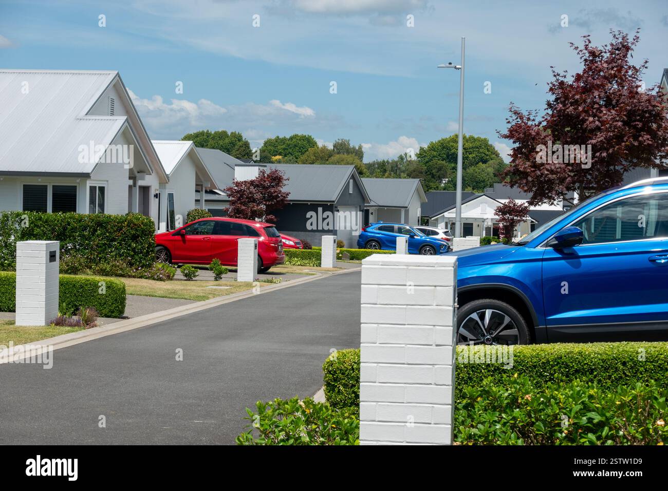 Strada residenziale di moderne case basse con auto rosse e blu luminose parcheggiate nei vialetti Foto Stock