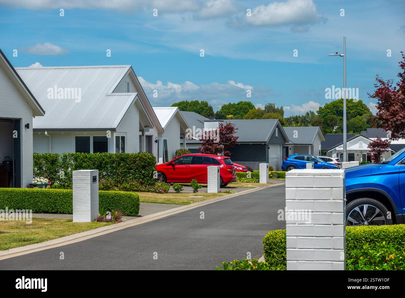 Strada residenziale di moderne case basse con auto rosse e blu luminose parcheggiate nei vialetti Foto Stock