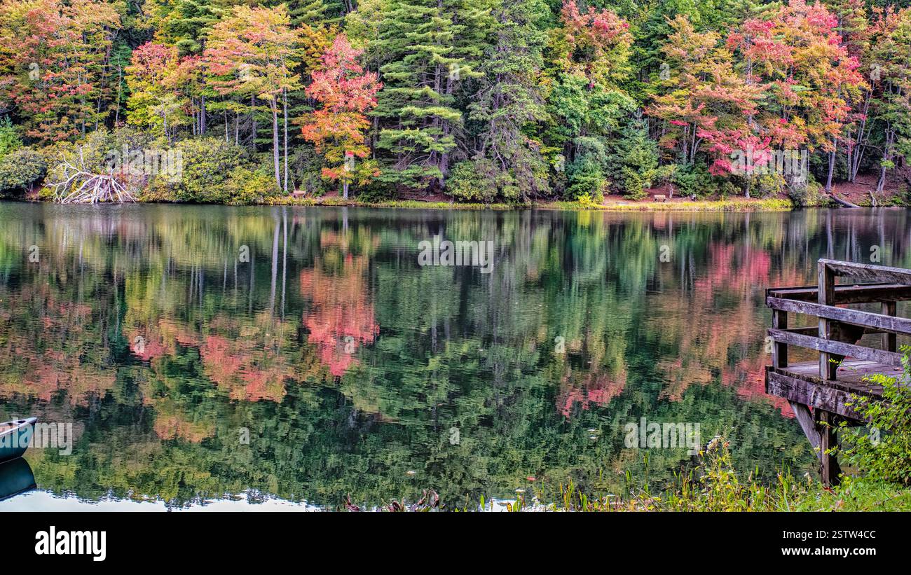 I colori vivaci del fogliame autunnale si riflettono su un lago fermo, creando un effetto simmetrico simile a uno specchio del paesaggio stagionale. Foto Stock