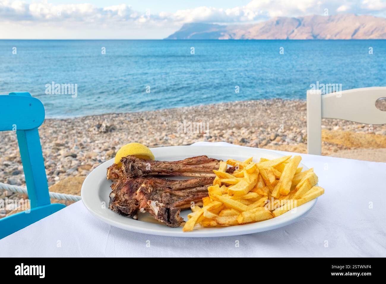 Costolette di agnello grigliate con patatine fritte su un tavolo nella taverna sul mare. Creta, Grecia. Foto Stock