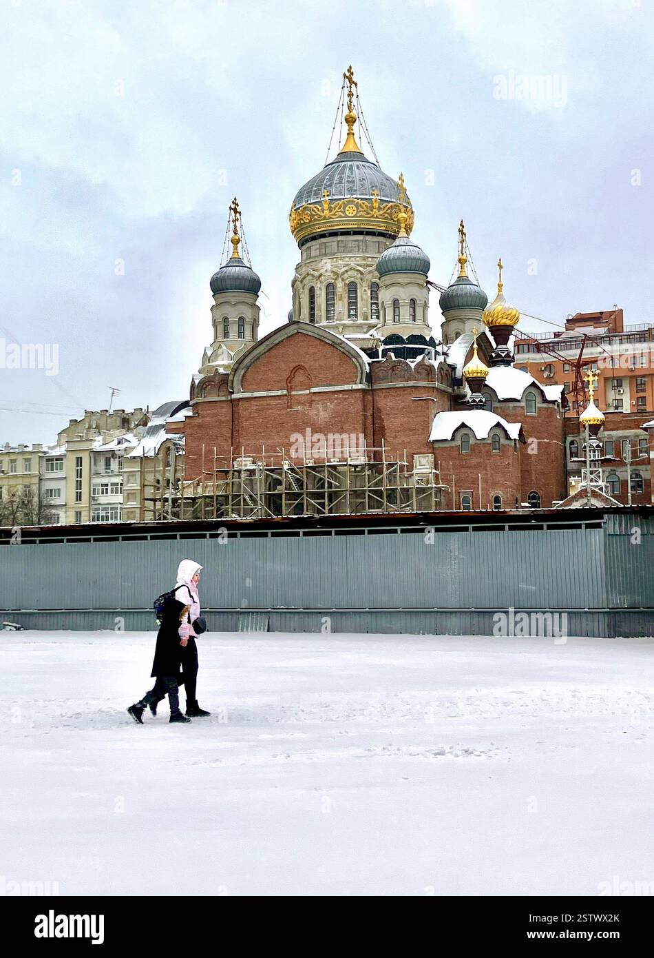 Una madre e suo figlio camminano attraverso la neve di fronte alla Chiesa della Santissima Trinità a Kiev il 27 novembre 2023. Foto Stock