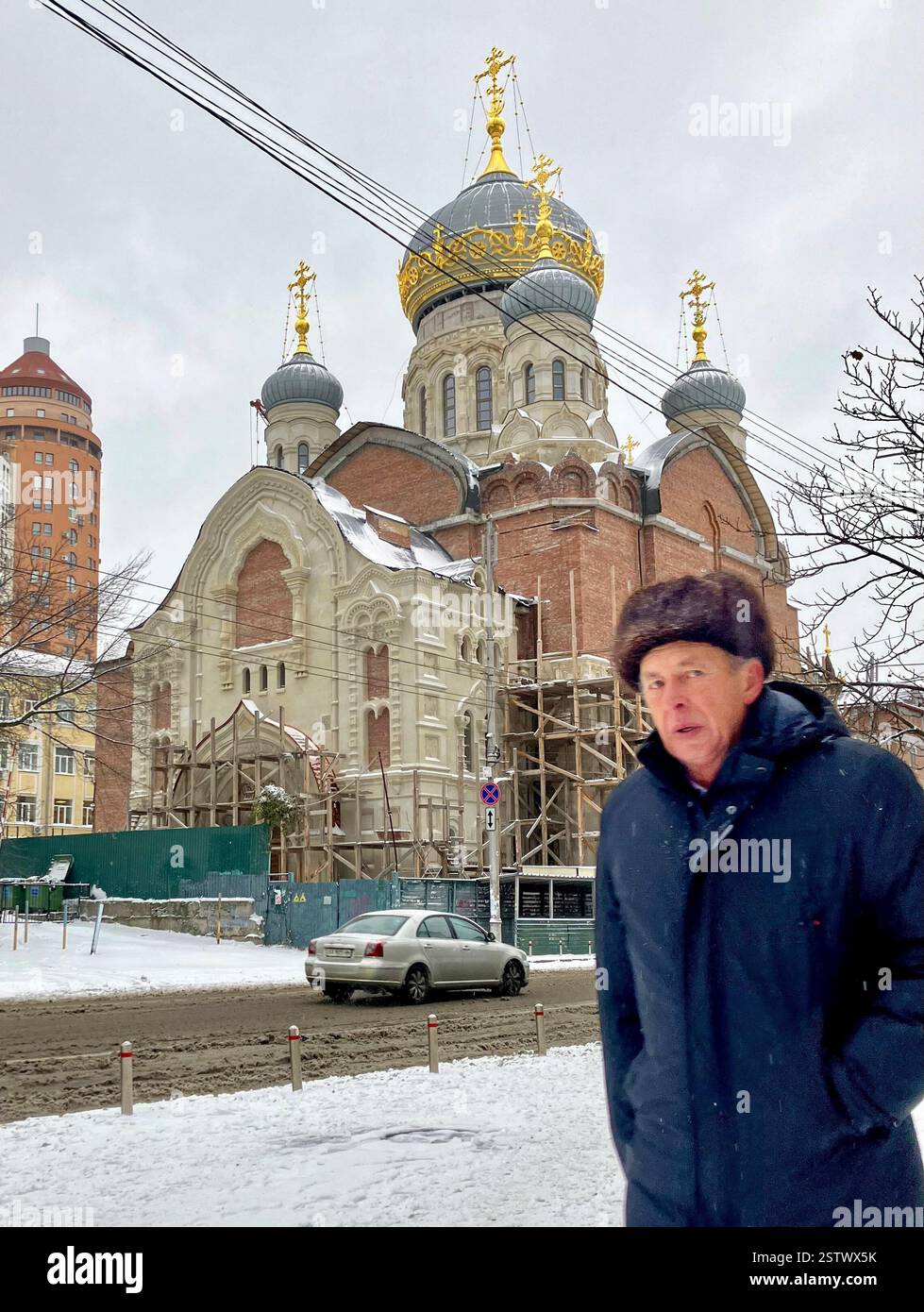 Un uomo cammina attraverso la neve di fronte alla Chiesa della Santissima Trinità a Kiev il 27 novembre 2023. Foto Stock
