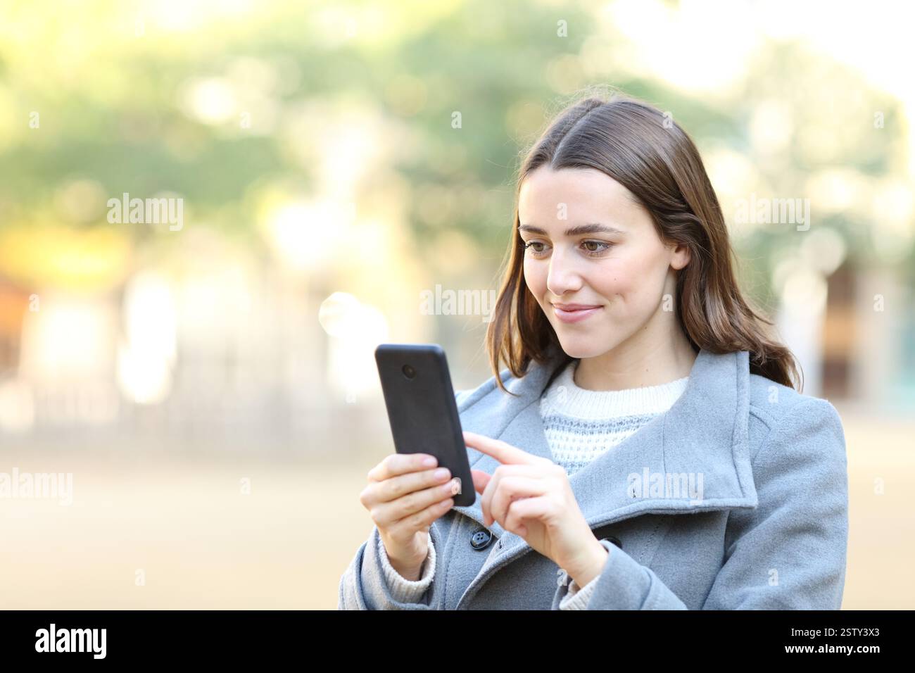 Donna soddisfatta in inverno che usa il cellulare che cammina per strada Foto Stock