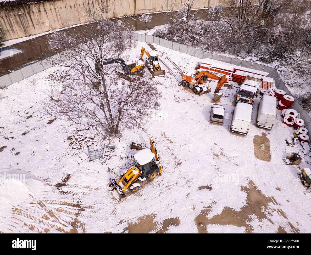 Vista aerea di un cantiere coperto di neve. Macchinari pesanti, escavatori e dumper rimangono fermi nel paesaggio invernale. Cingoli degli pneumatici in Foto Stock