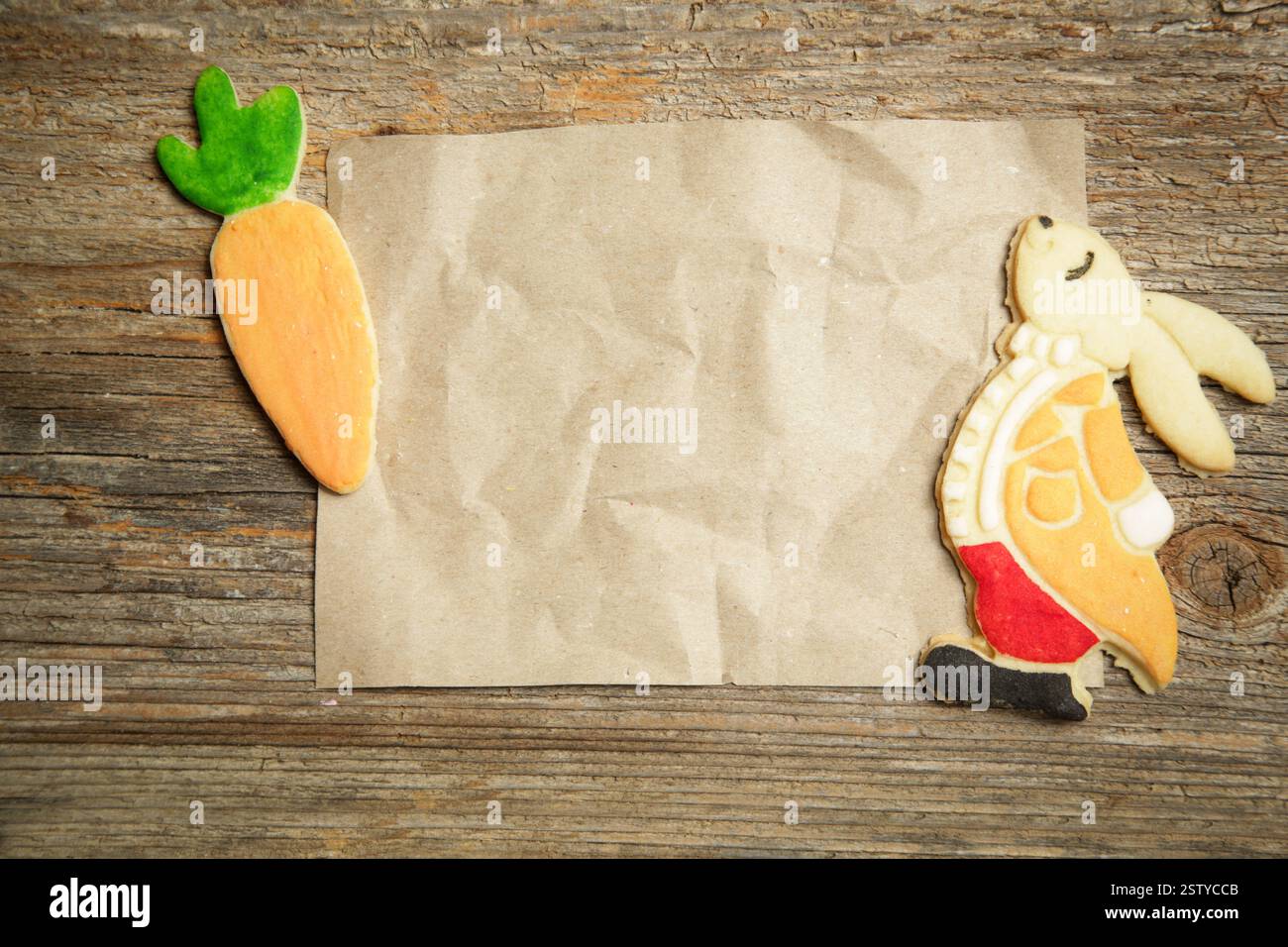 Vista dal tavolo dei biscotti pasquali sul tavolo in legno rustico con carta marrone vuota, preparatevi a preparare la ricetta di cottura. Foto Stock