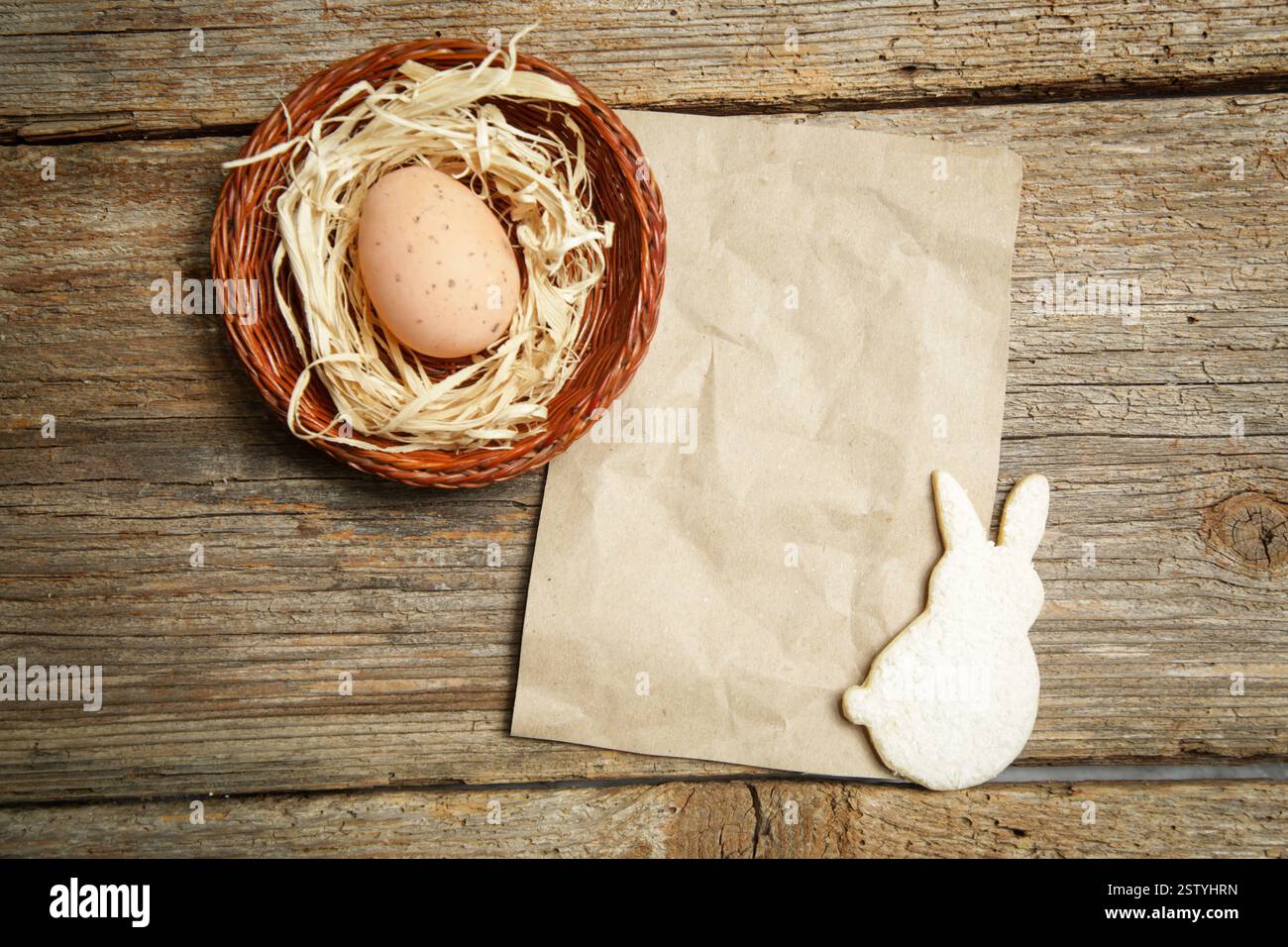 Vista sul tavolo dei biscotti di zucchero e delle uova di Pasqua in un nido su fondo rustico in legno con carta bianca, Mock Up per biglietti d'auguri o fornelli Foto Stock