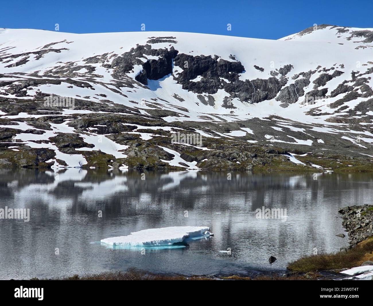 Serena riflessione delle montagne innevate sulle acque glaciali della Norvegia Wilderness Foto Stock