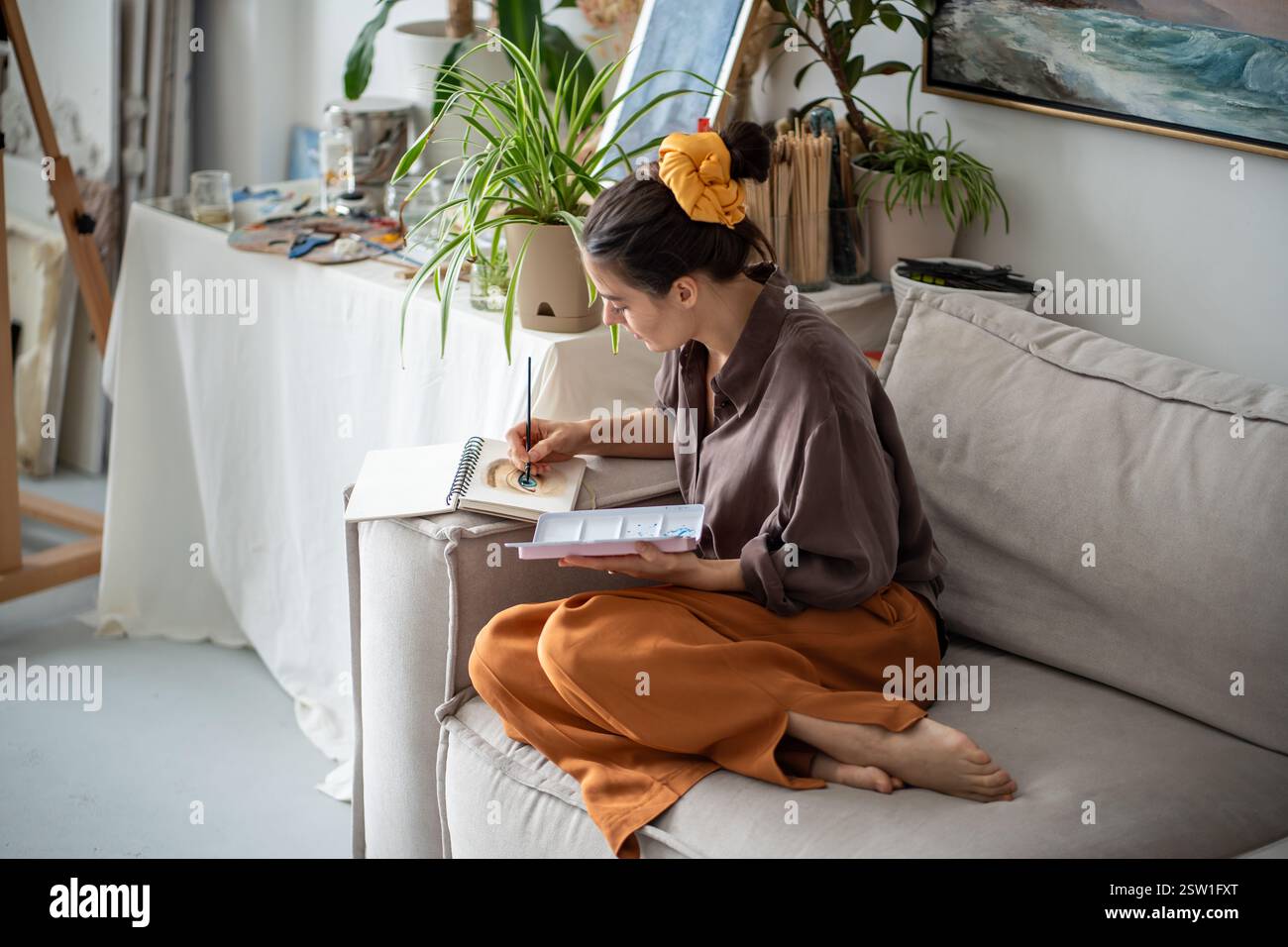 Donna artistica ispirata che disegna con calma e attenzione schizzi con pennello e vernici ad acquerello. Foto Stock