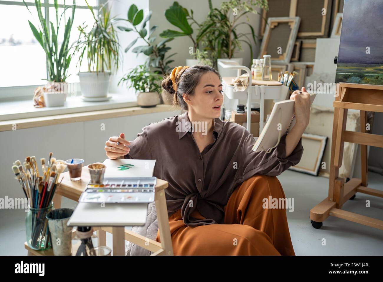 Artista femminile seduta sul pavimento dello studio d'arte domestico lettura studio manuale, pittura con aquarelle Foto Stock