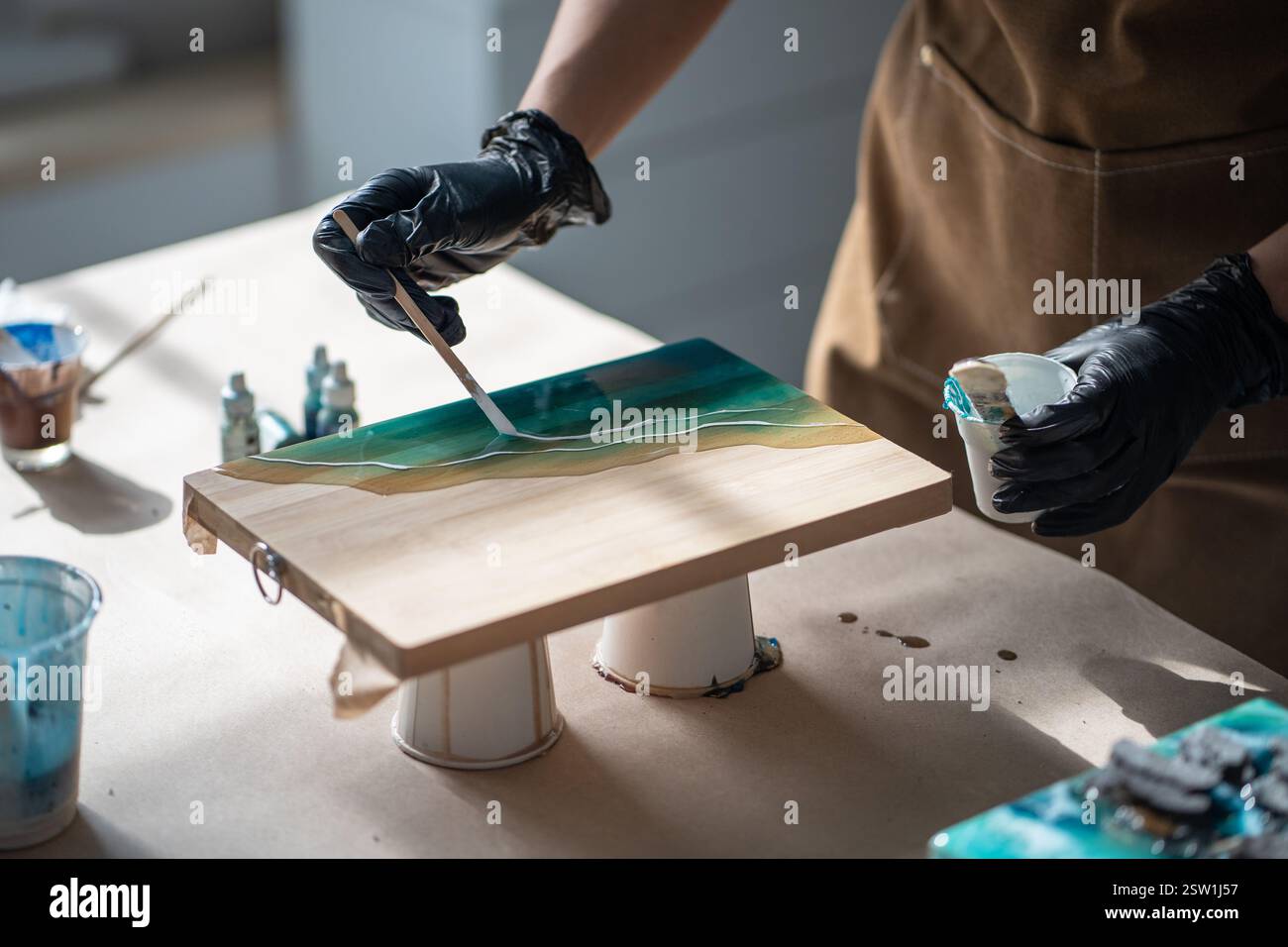 Le mani di un'attenta artista femminile elaborano i dettagli della pittura, creando opere d'arte in resina epossidica. Foto Stock