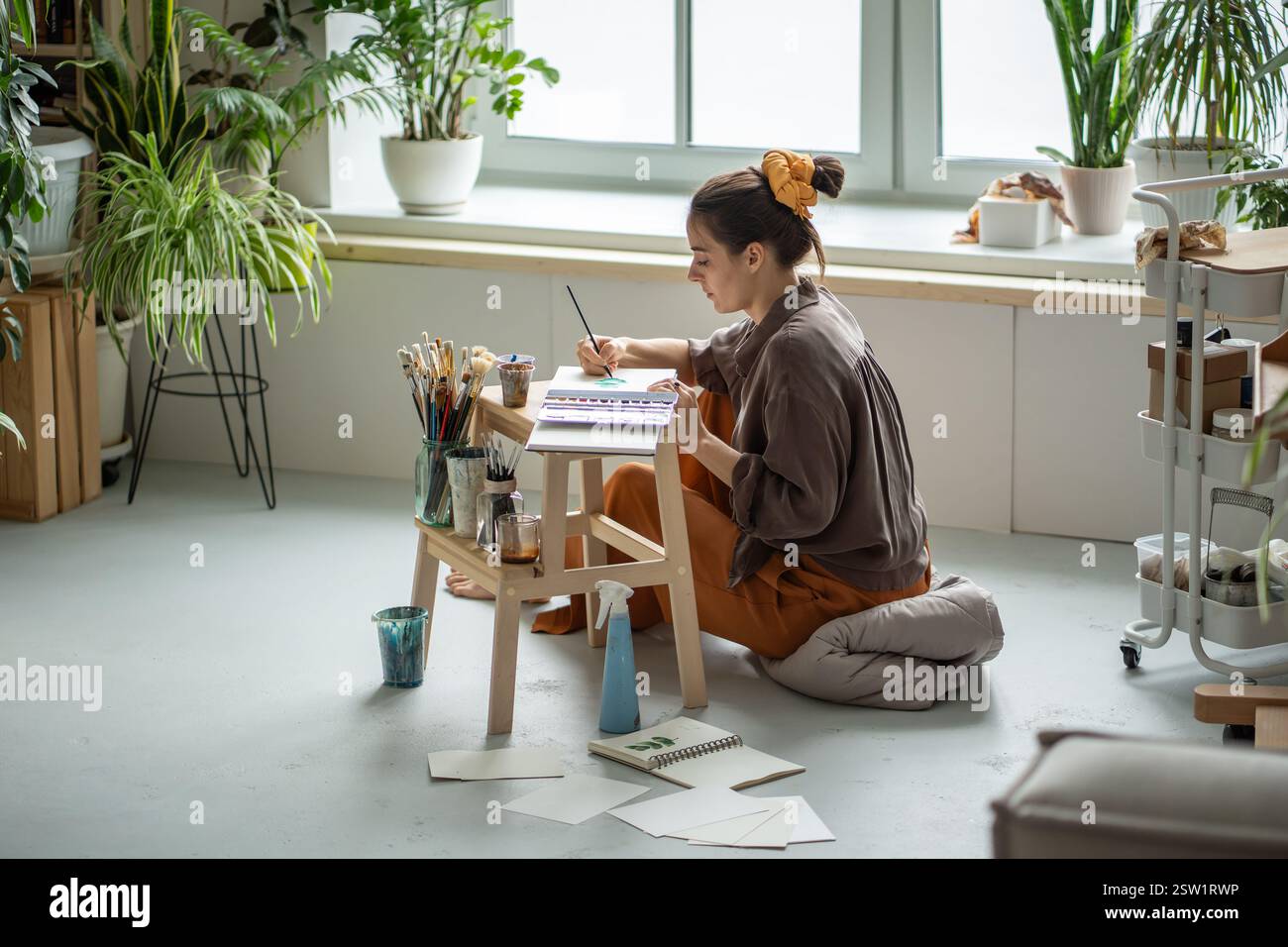 Donna artistica concentrata che lavora con attenzione a piccoli schizzi con pennelli ad acquerello Foto Stock