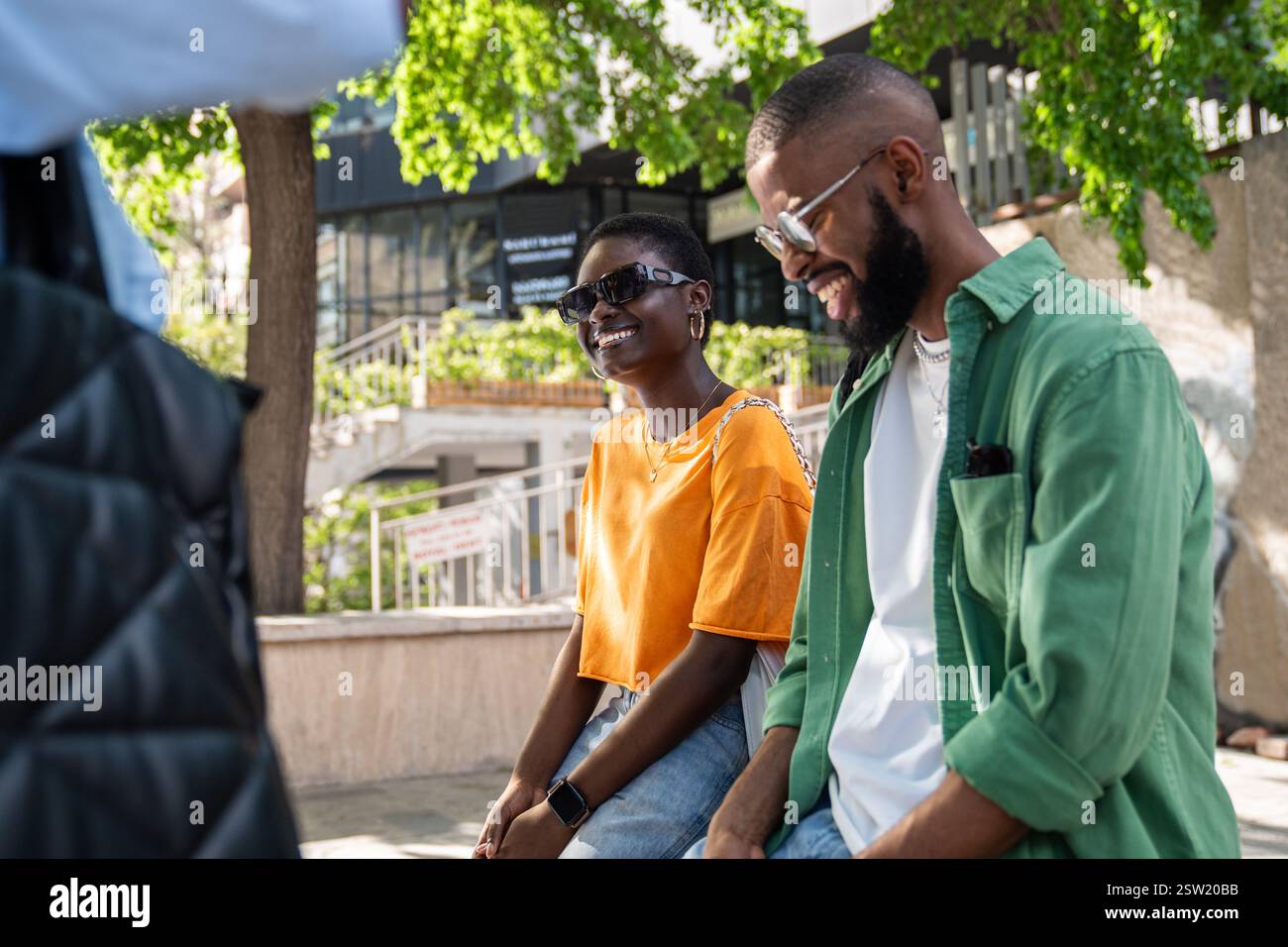 Ridendo gioioso ragazzo afroamericano e ragazza seduti fuori a conversare con gli amici. Foto Stock
