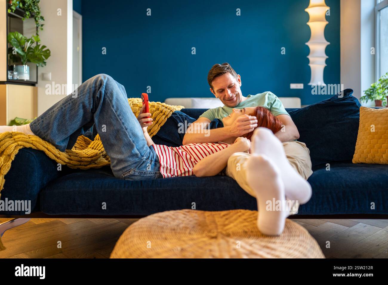 Donna felice e rilassata sdraiata con lo smartphone sulle ginocchia del marito Foto Stock
