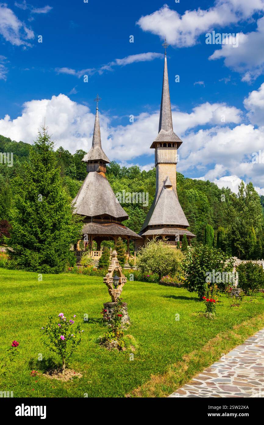 Vista di alte torri in legno e di un giardino fiorito, tipica architettura in legno nel Monastero di Barsana, Romania. Foto Stock