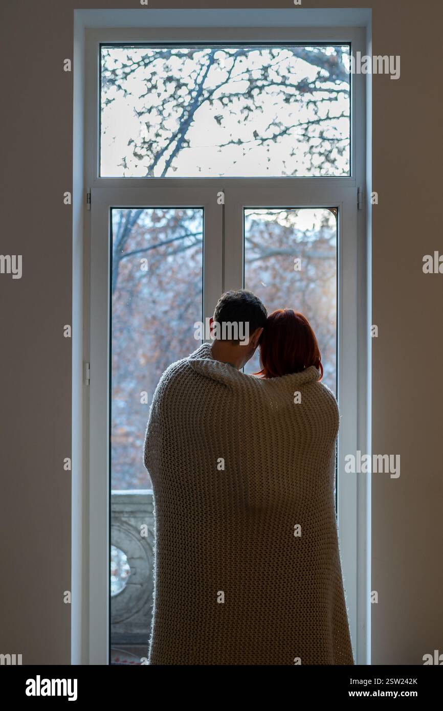 Coppia avvolta in coperta che guarda fuori finestra Foto Stock