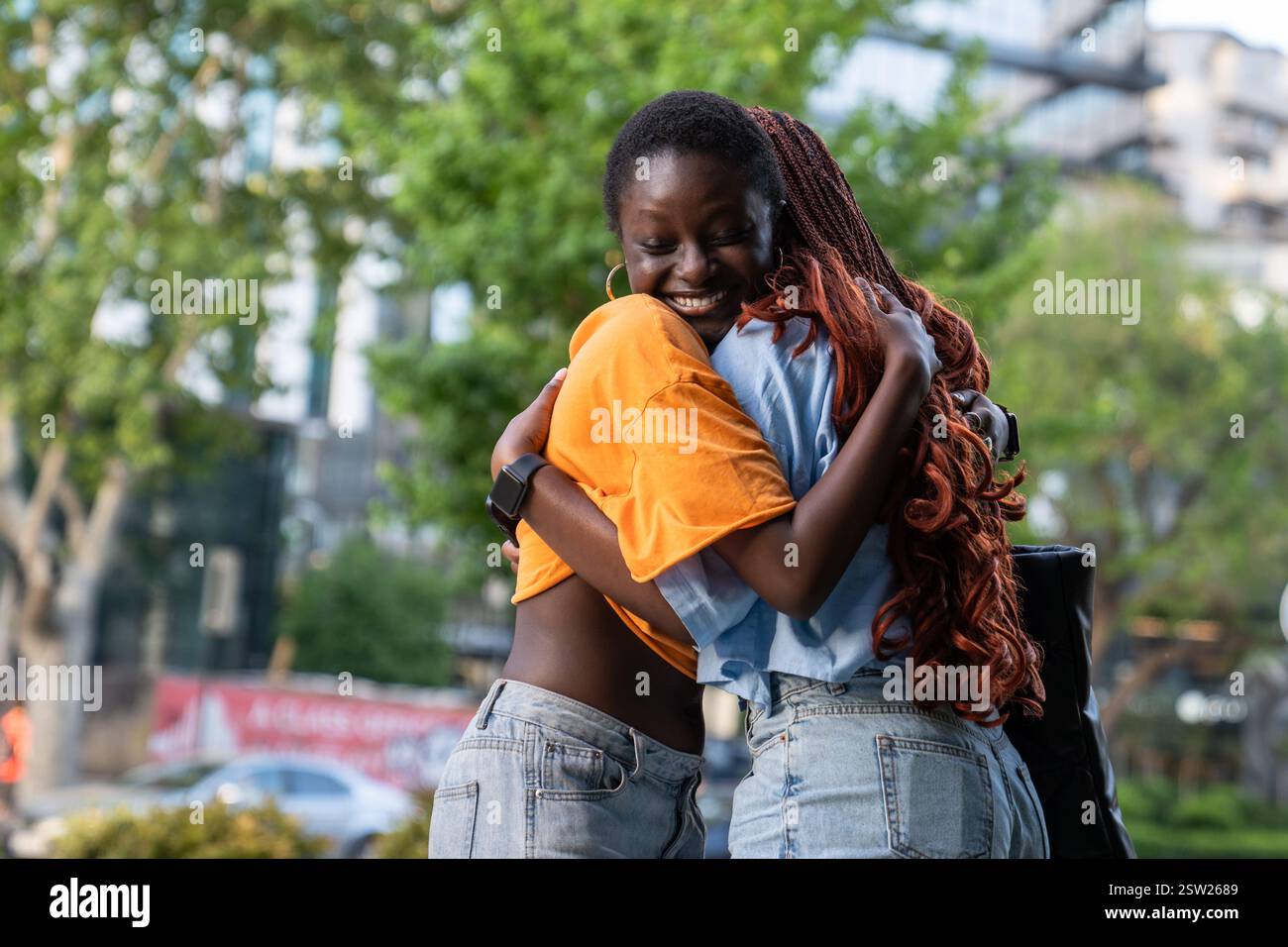 Donne afroamericane gioiose e allegre che abbracciano con amore, sorridono felicemente fuori di strada Foto Stock