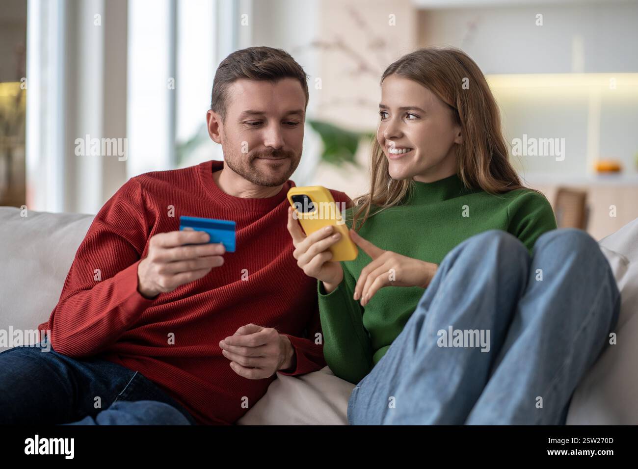 Shopping online a casa. La coppia interessata paga gli acquisti con carta di credito utilizzando il telefono seduto sul divano. Foto Stock