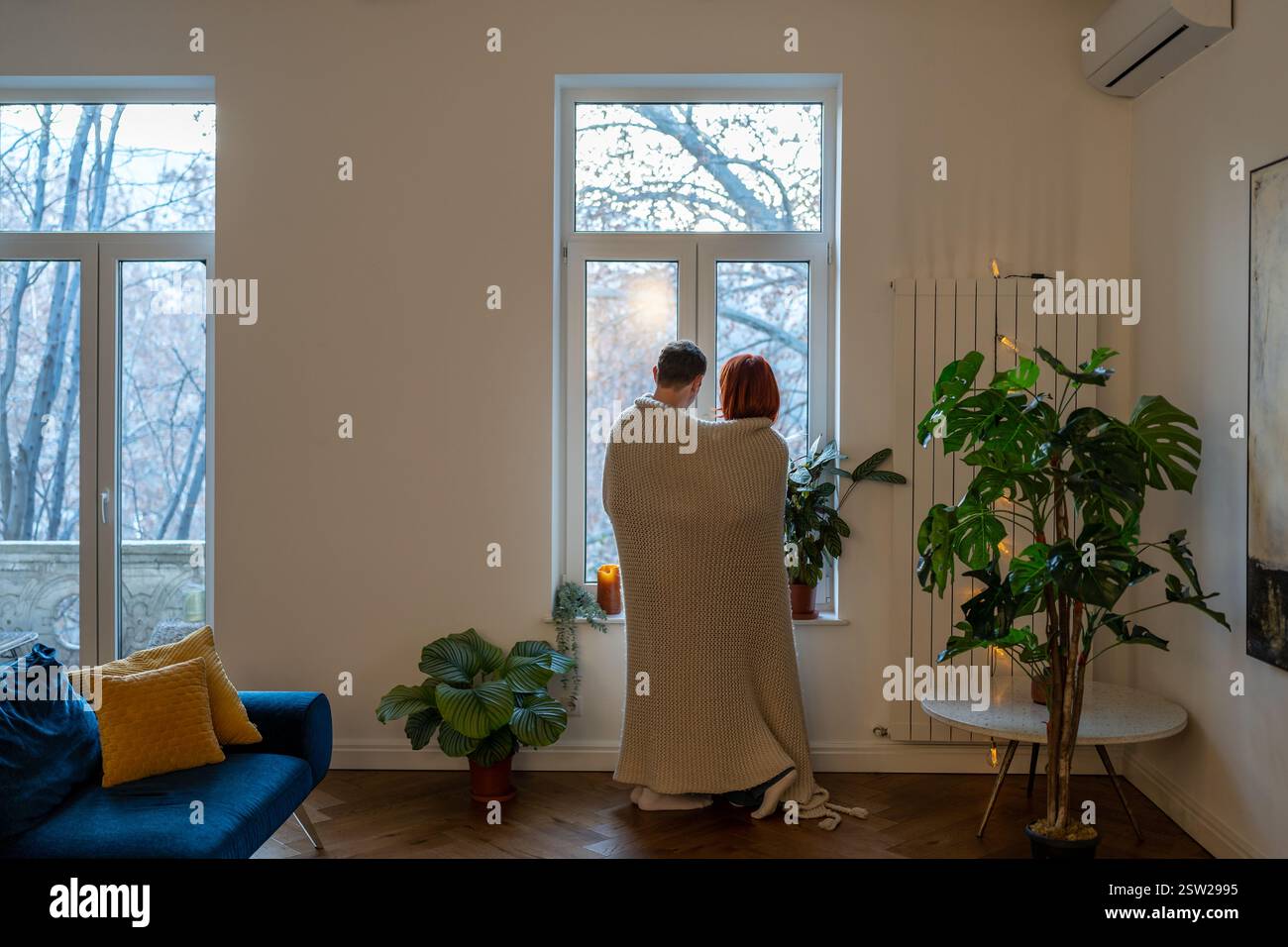 Famiglia coppia moglie marito abbraccio guardando la finestra in piedi nel soggiorno a casa. Foto Stock