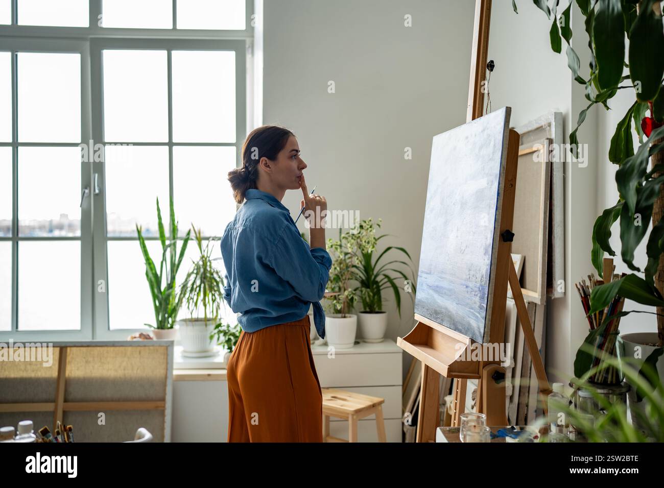 Valutazione grafica in officina. Artista donna premurosa che esamina la pittura in una brillante galleria d'arte Foto Stock