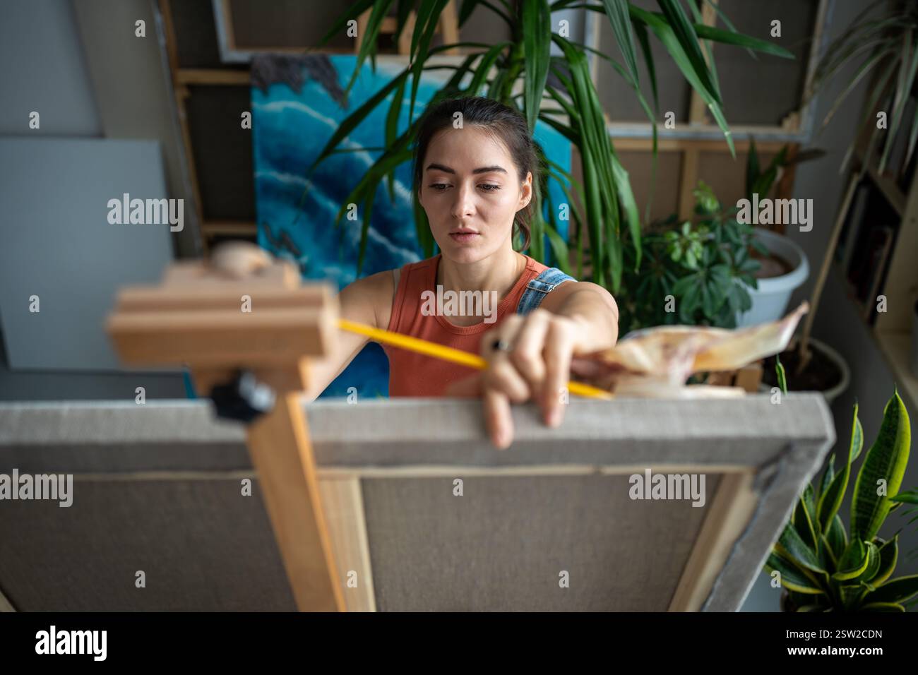 Artista donna orgogliosa e fiduciosa che dipinge un quadro in uno studio di arte leggera. Processo creativo. Foto Stock