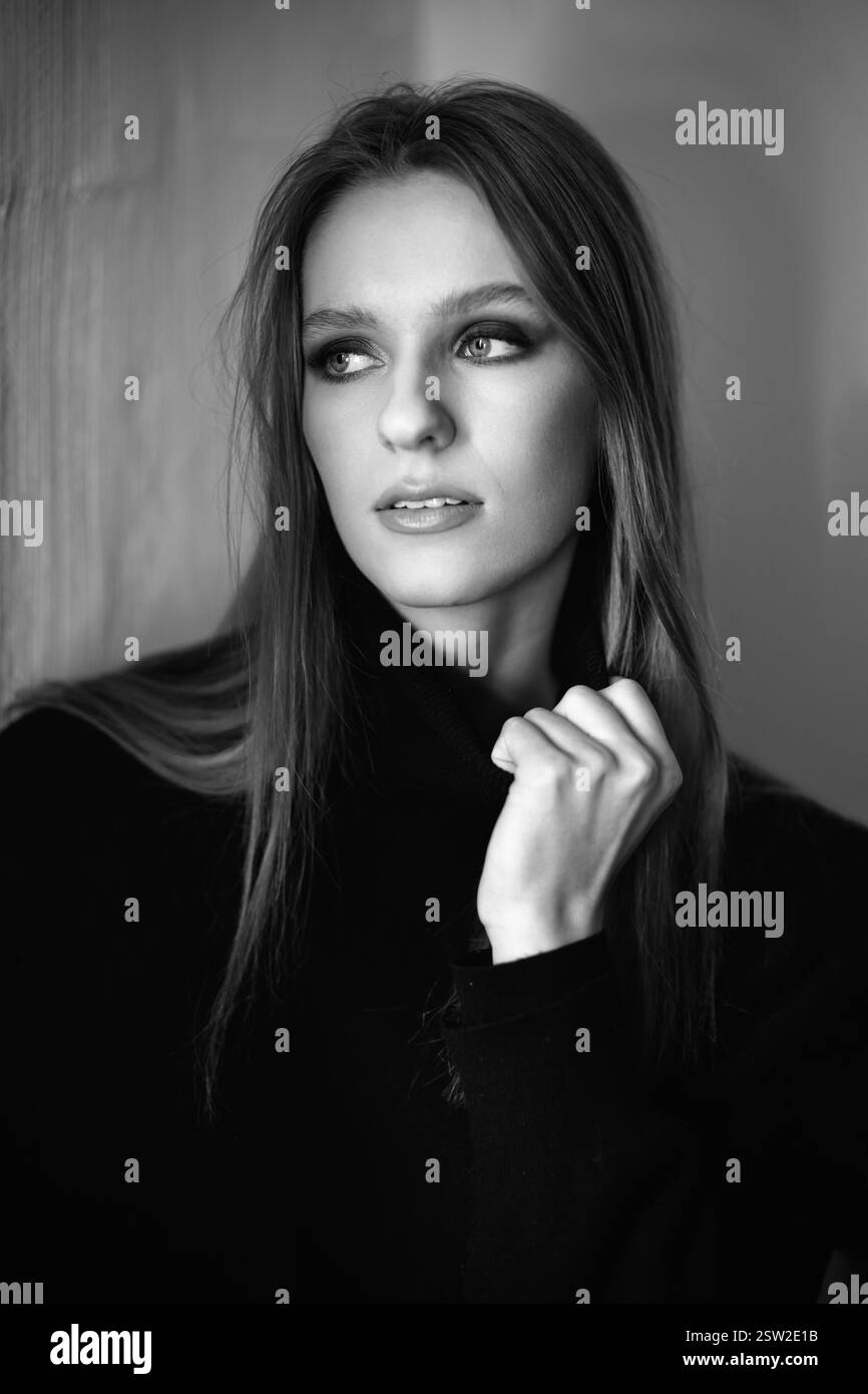 Il ritratto in bianco e nero cattura una donna con un maglione nero, con luce soffusa. Il suo sguardo sicuro e il delicato gesto della mano creano un elegante, cinematografico, a Foto Stock