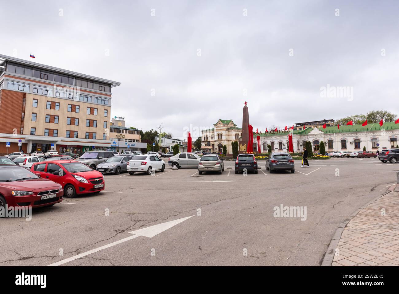 Essentuki, Russia - 9 maggio 2023: Vista sulla strada con auto parcheggiate vicino alla stazione ferroviaria centrale in Piazza della stazione decorata con bandiere rosse in onore del d Foto Stock