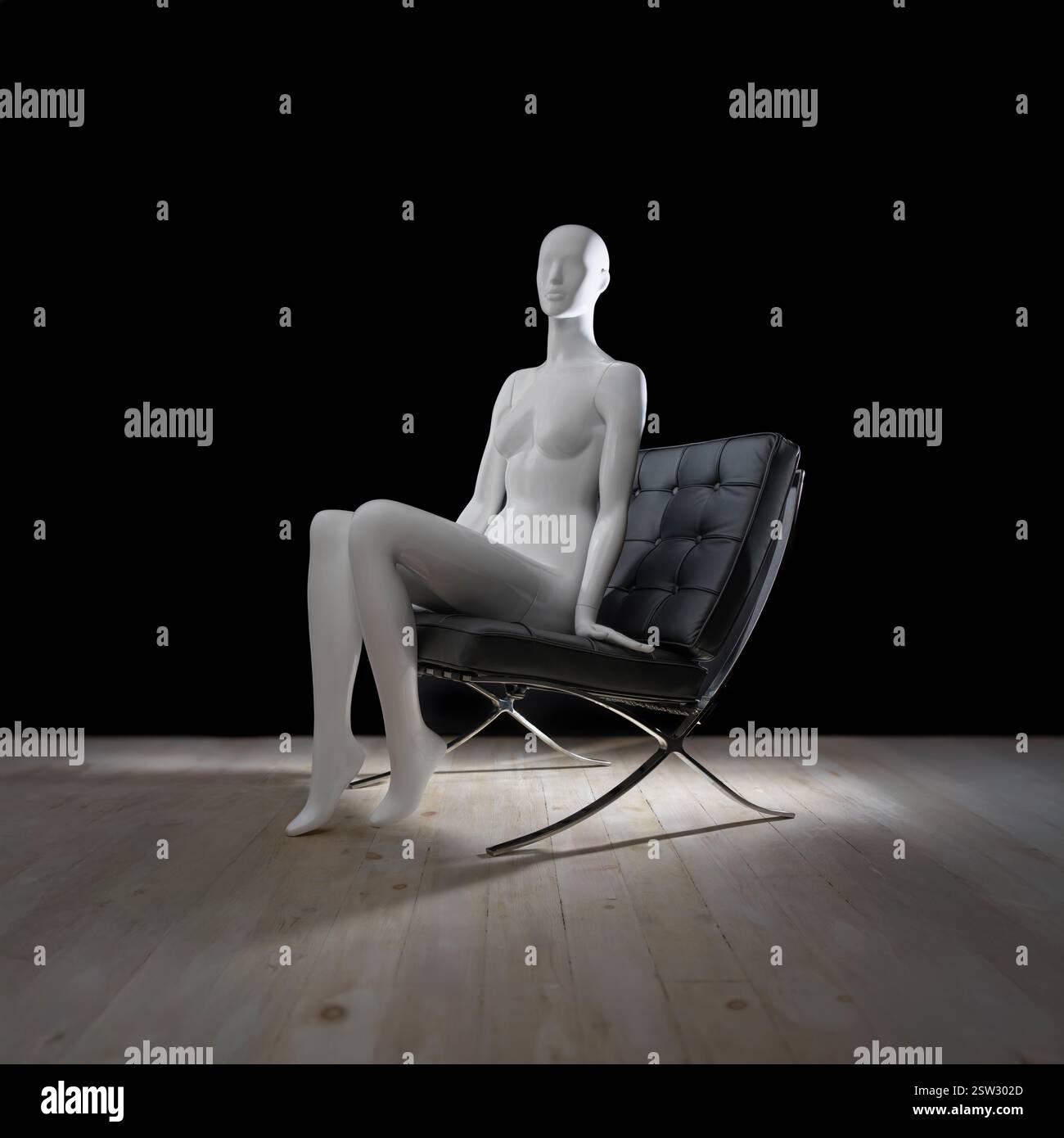 Manichino femminile bianco seduto su un'elegante sedia in pelle nera in uno spazio poco illuminato, sottolineandone il design elegante. Foto Stock
