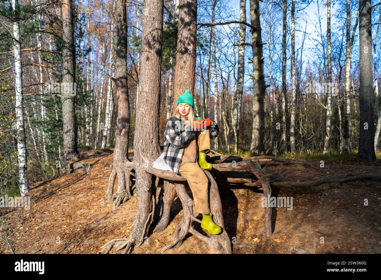 Una donna rilassata e sognante con abiti caldi seduto con una tazza di tè caldo all'aperto circonda alberi autunnali nella foresta Foto Stock