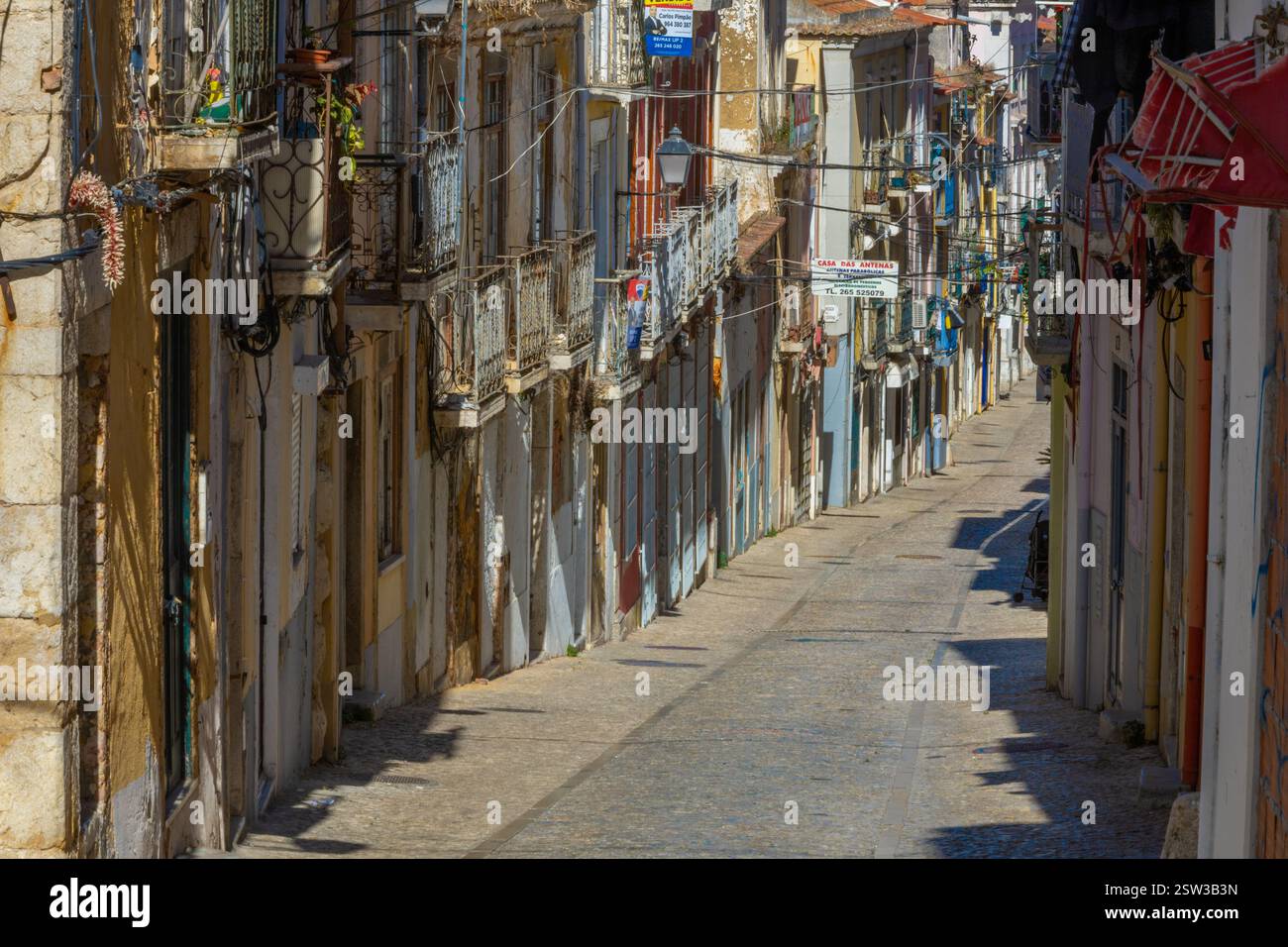 Una tipica vecchia strada europea, stretta con i suoi antichi edifici, la città europea. Un paesaggio urbano di Setúbal con minuscoli negozi e caffetterie. Foto Stock