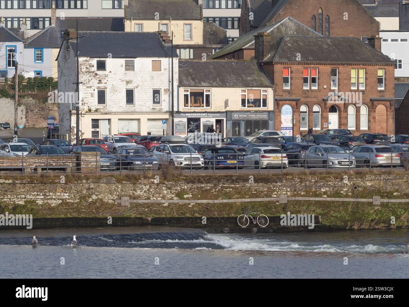 Vista sul fiume Nith fino alle Whitesands, al centro di Dumfries, Scozia. Parcheggio in primo piano, diversi stili di edificio alle spalle. Foto Stock