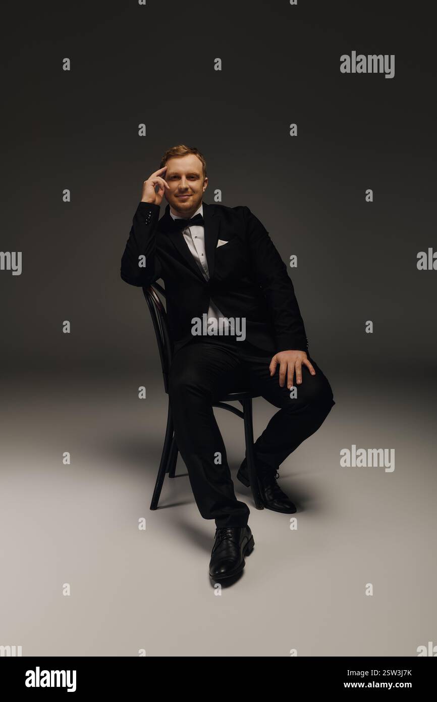 Un bell'uomo siede con fiducia in uno studio, vestito impeccabilmente con un smoking e un papillon. Foto Stock