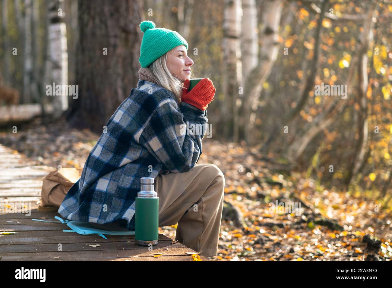 Tempo da solo. Rilassata donna di mezza età goditi un fine settimana tranquillo nel parco autunnale con bevande meditative, tè thermos. Foto Stock