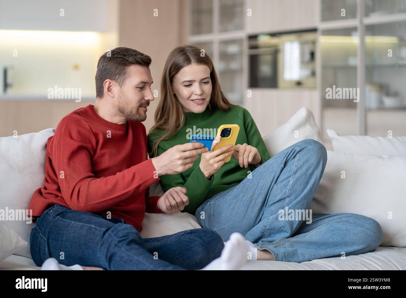 Shopping online a casa. La coppia interessata paga gli acquisti con carta di credito utilizzando il telefono seduto sul divano. Foto Stock