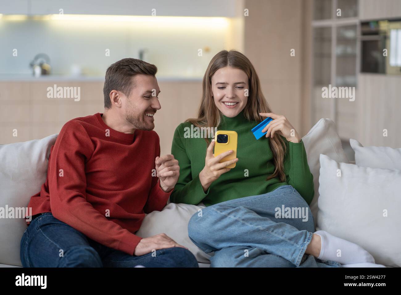 Shopping online a casa. La coppia interessata paga gli acquisti con carta di credito utilizzando il telefono seduto sul divano. Foto Stock