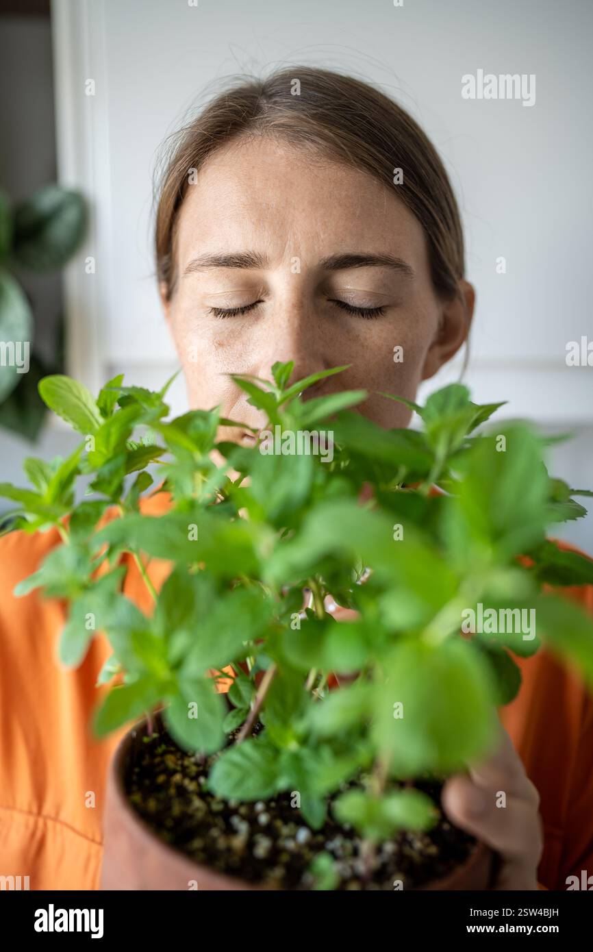 Primo piano di donna a occhi chiusi godendo di profumata pianta di menta verde che la coltiva a casa. Hobby verde Foto Stock