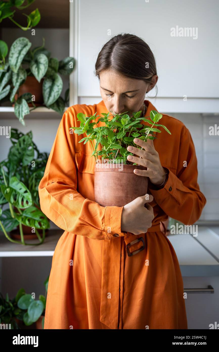 Donna a occhi chiusi che gode di un odore di menta verde in cucina a casa. Amante delle piante domestiche. Foto Stock
