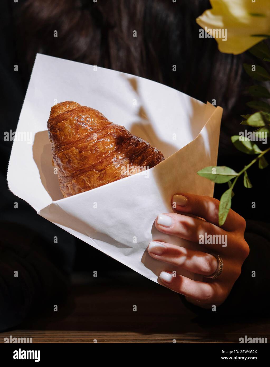 Donna che tiene in mano un croissant al bar Foto Stock