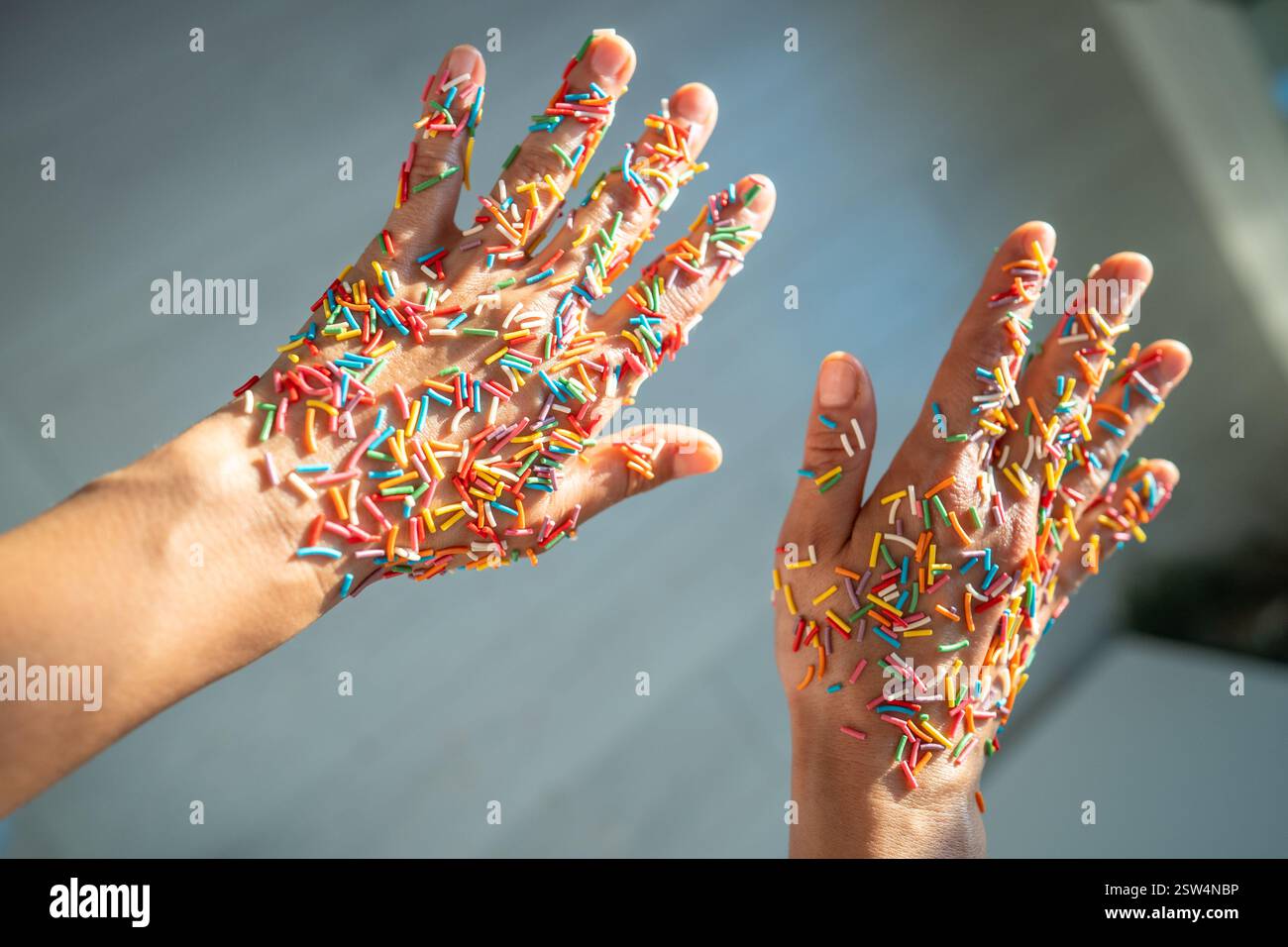 Torte fatte in casa senza zucchero con sprinkles. Mani appiccicose femminili in coloratissimi sprinkles, dessert di caramelle Foto Stock