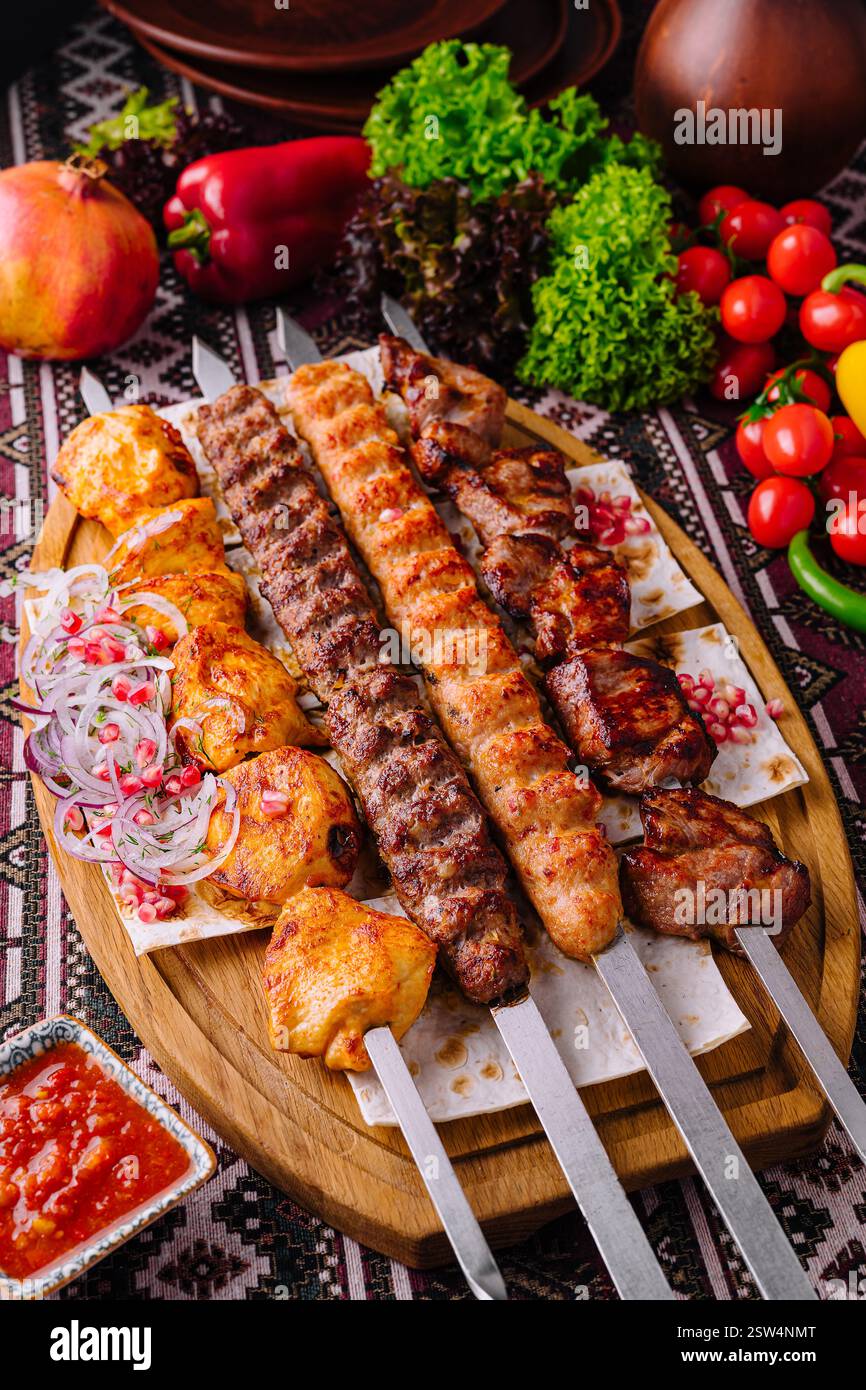 Appetitosa presentazione di spiedini assortiti alla griglia su un tavolo di legno con verdure fresche Foto Stock