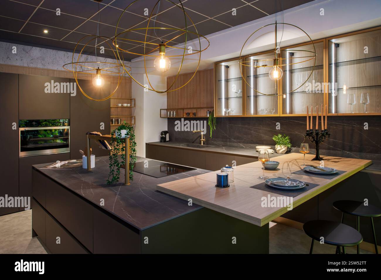 Cucina contemporanea dal design elegante, elettrodomestici integrati e un'isola centrale illuminata da luci a sospensione sferiche Foto Stock