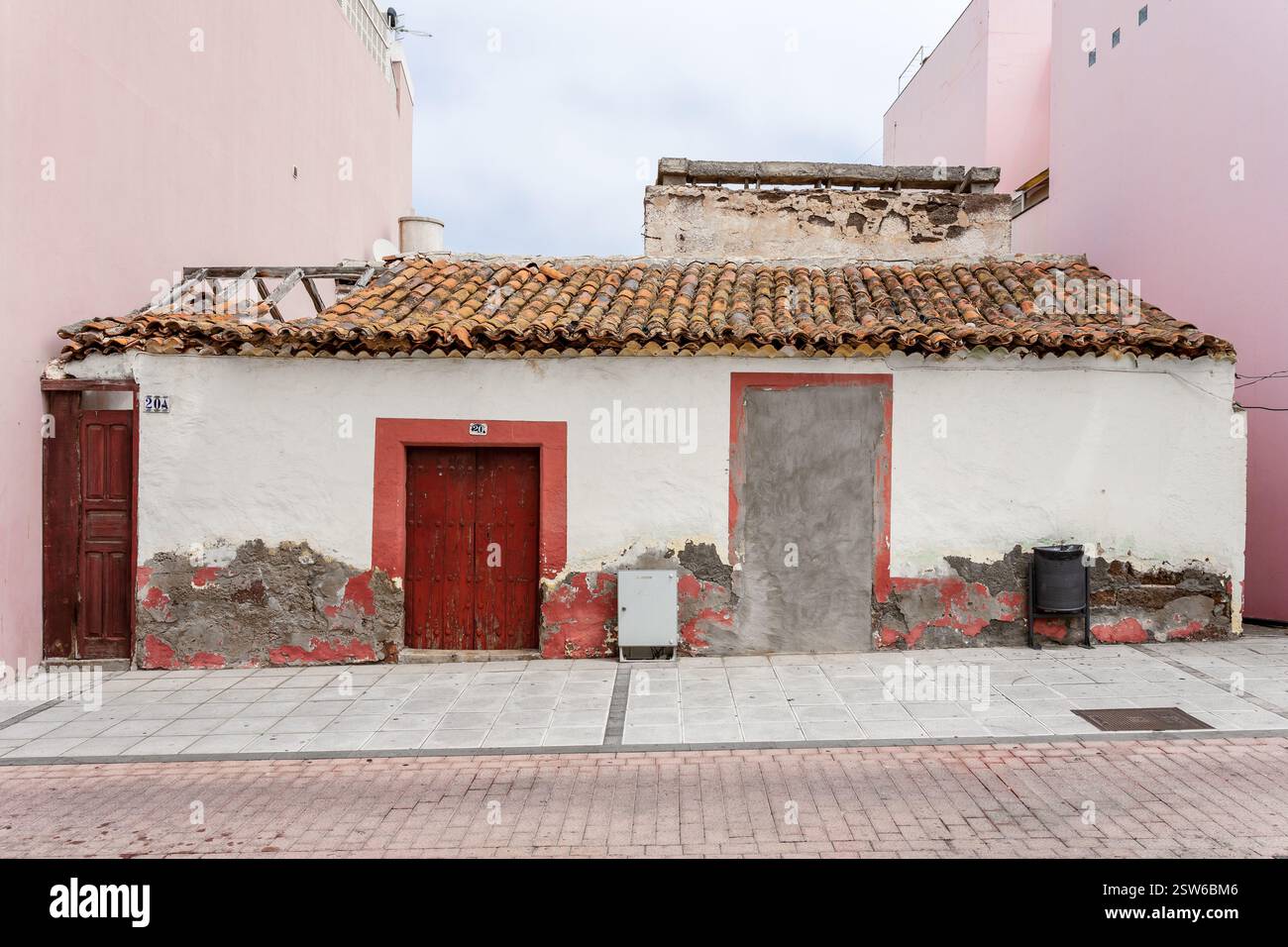 Un vecchio edificio con un tetto piastrellato, porte rosse e muri che si staccano. Foto Stock