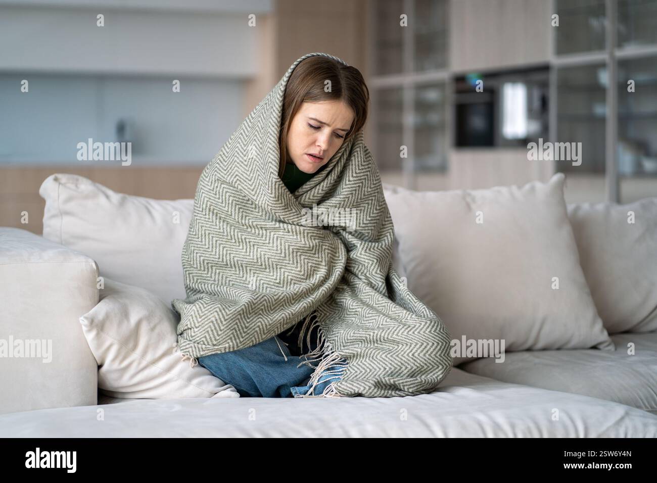 Donna depressa seduta sul divano avvolta in coperta, sente solitudine, tristezza, affaticamento emotivo, pms Foto Stock
