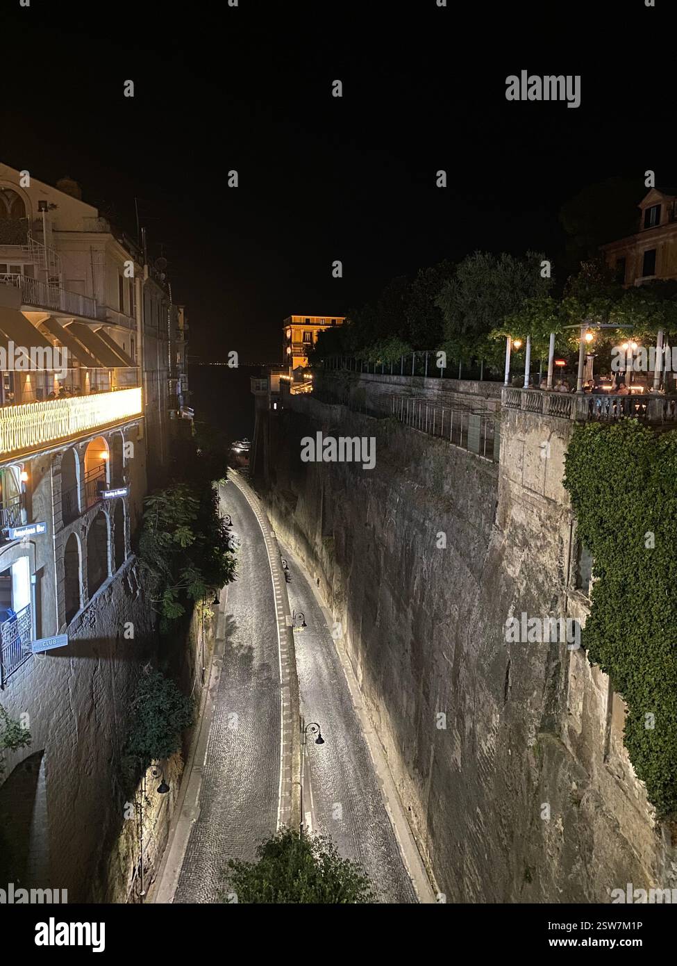 Una strada panoramica acciottolata a Sorrento, in Italia, illuminata di notte, circondata da edifici storici e vegetazione lussureggiante. - Immagine stock catturata con smartphone