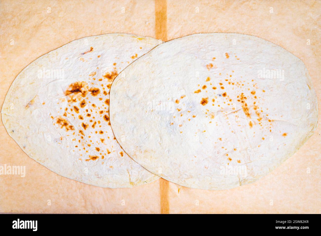 Due tortillas rotonde e leggermente carbonizzate poggiano su una semplice superficie di legno. La loro consistenza calda e le sottili macchie dorate mostrano che sono state cotte di recente, Foto Stock