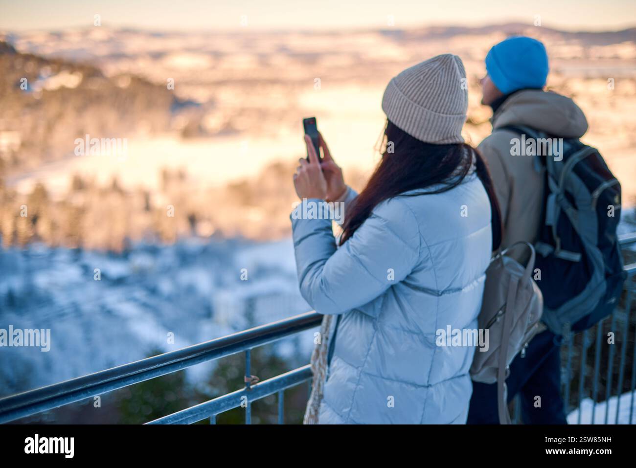 Questa immagine vibrante mostra una viaggiatrice impegnata nella fotografia su smartphone su uno sfondo urbano panoramico. La donna, probabilmente sui 30 anni, sta in piedi Foto Stock