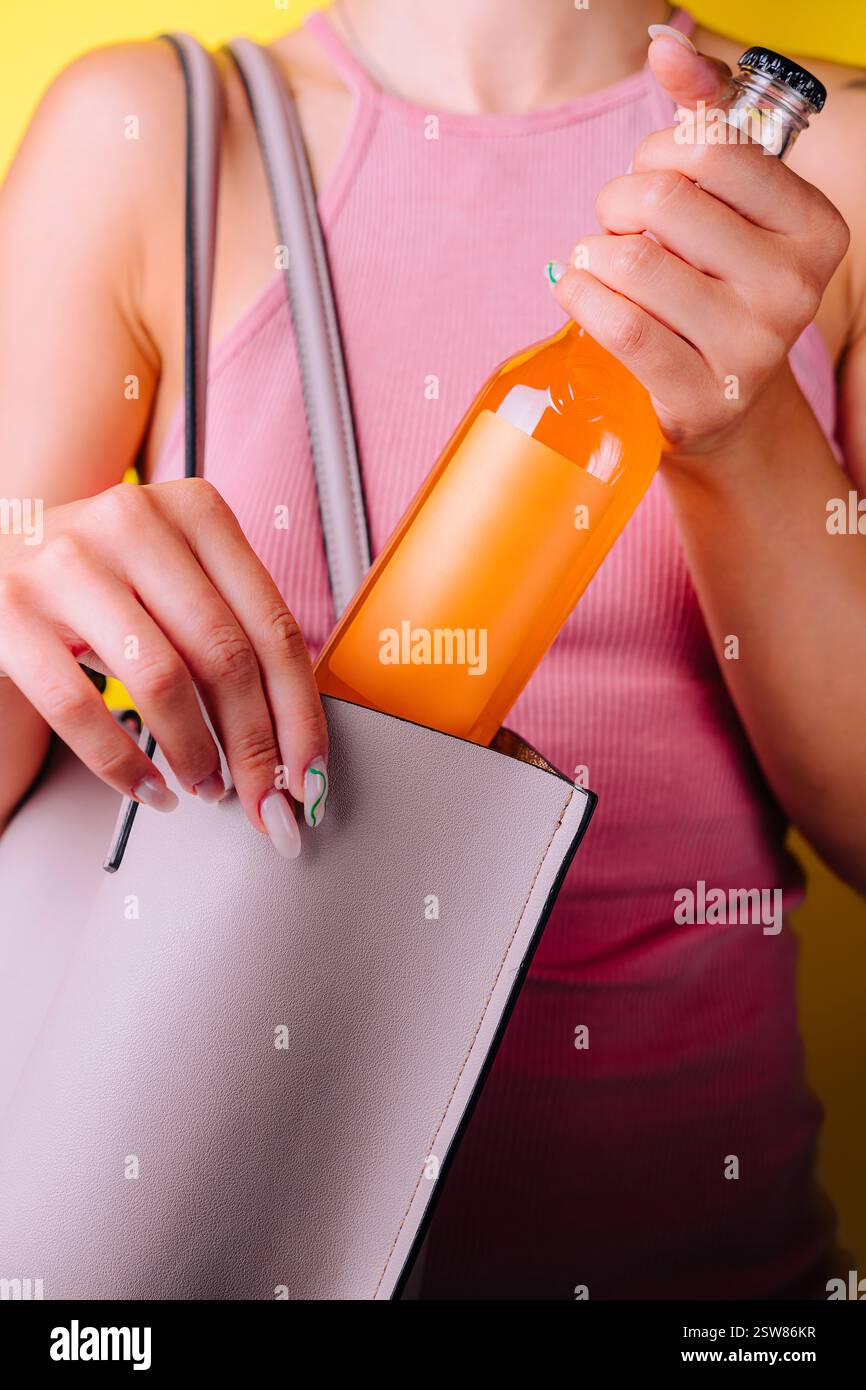 Donna che nasconde la bottiglia di succo d'arancia nella sua borsa su sfondo giallo Foto Stock
