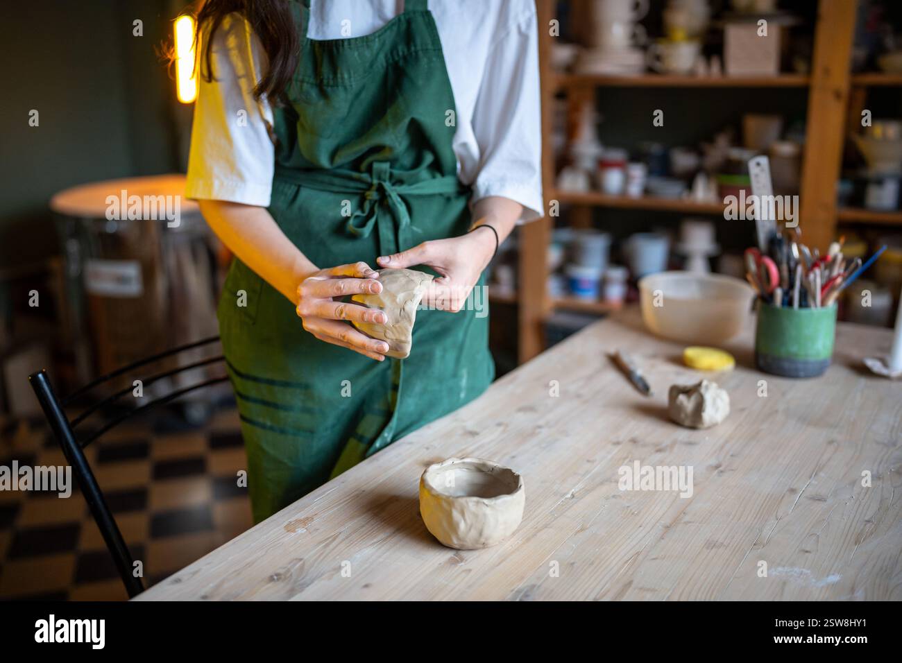 Le mani di donna potter modellano una ciotola di argilla bianca su un tavolo illuminato da candele di legno nello studio di laboratorio di ceramica Foto Stock