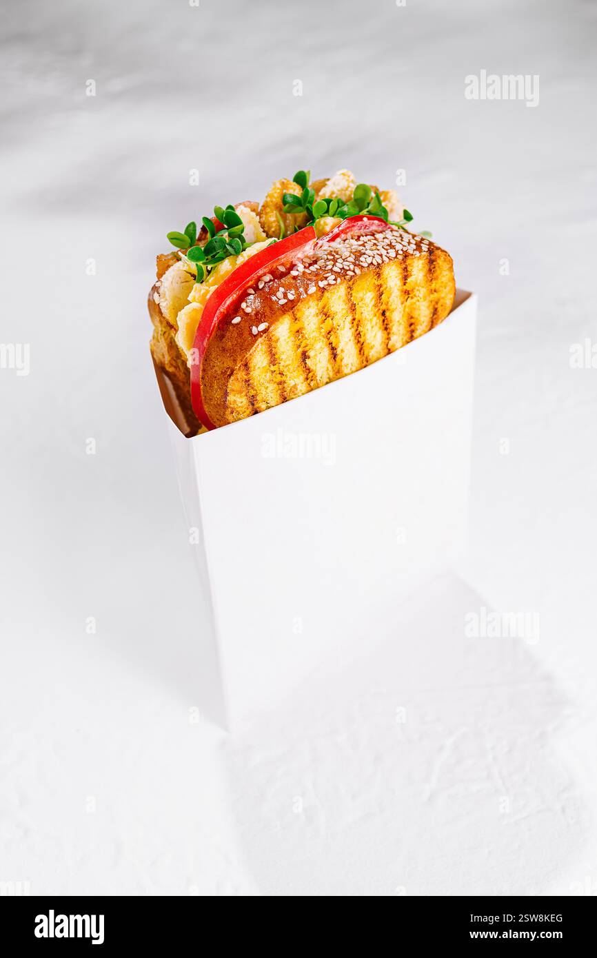 Delizioso panino tostato con pollo e verdure in scatola di cartone bianca su sfondo bianco Foto Stock