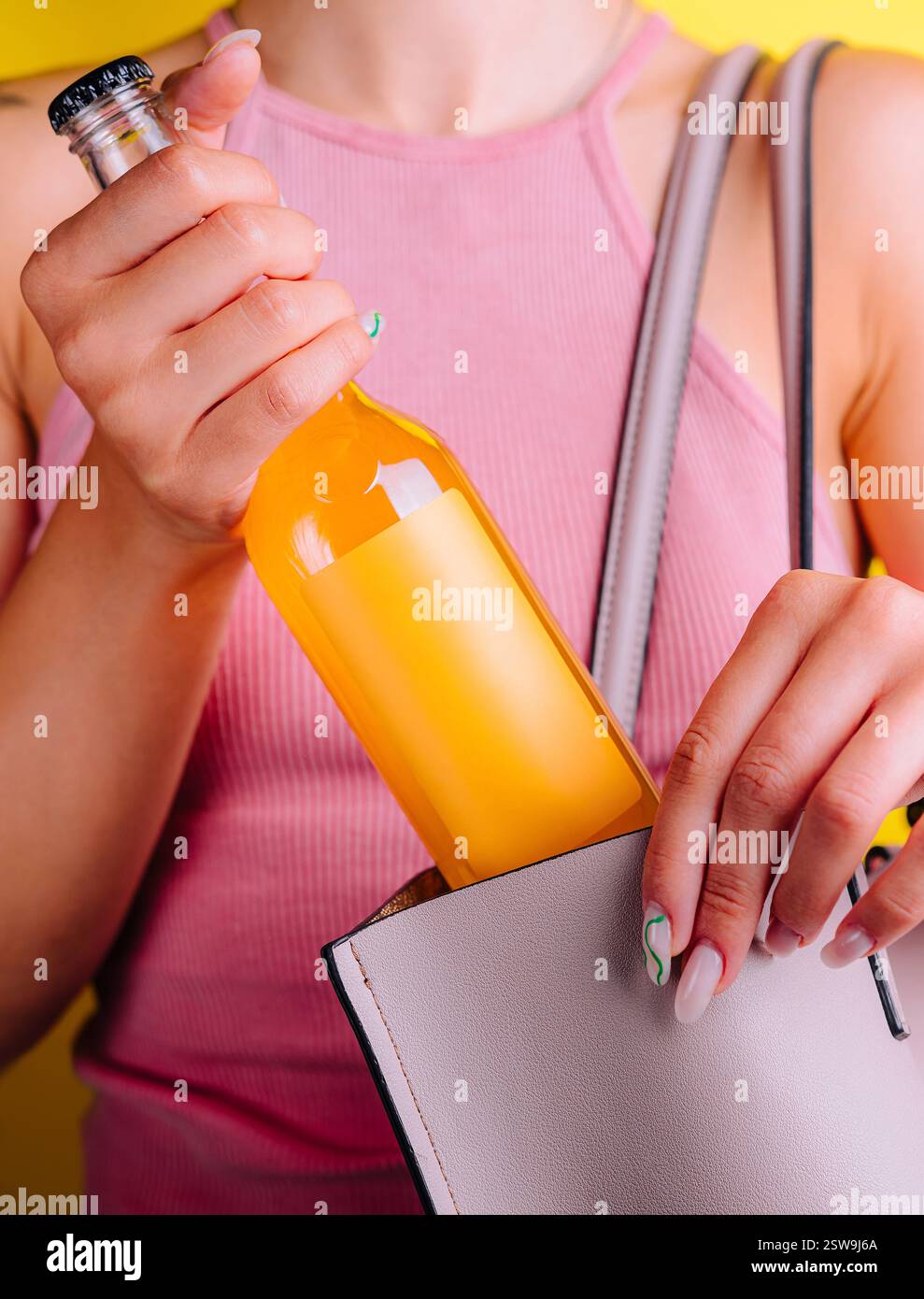 Donna che nasconde la bottiglia di succo d'arancia nella sua borsa su sfondo giallo Foto Stock
