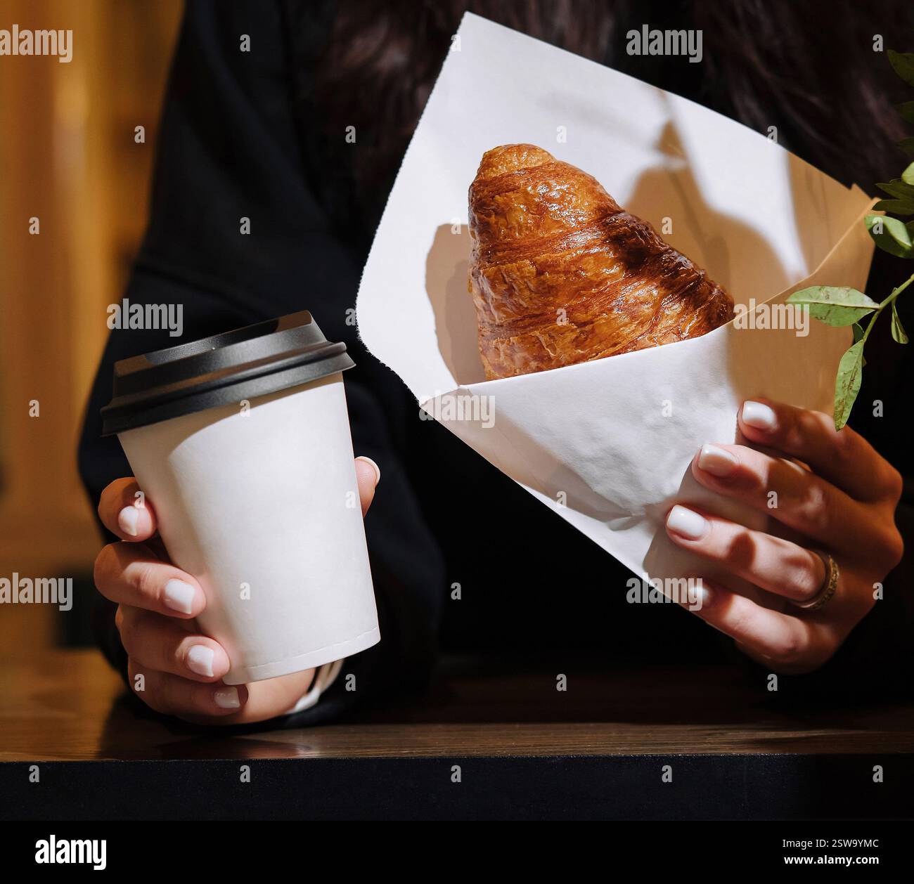 Donna che tiene caffè e croissant in caffetteria Foto Stock